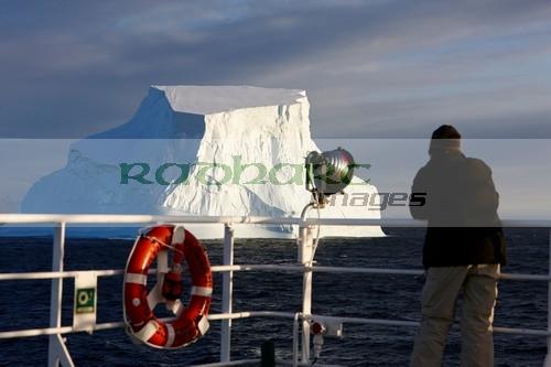 man taking photograph of giant iceberg on board ship in antarctica