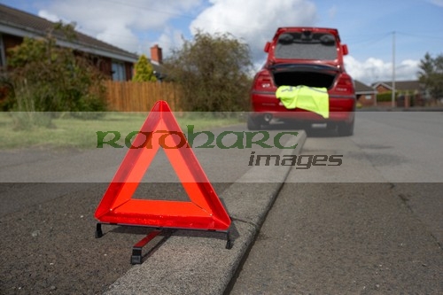 hazard warning triangle laid out on the side of the road in a residential area behind a broken down car